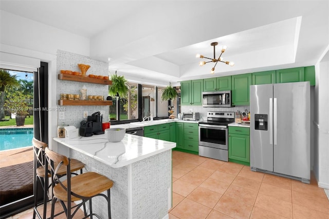 kitchen with green cabinets, stainless steel appliances, kitchen peninsula, and a tray ceiling