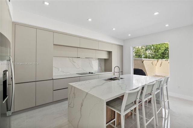 kitchen featuring light stone counters, sink, decorative backsplash, a breakfast bar, and a center island with sink