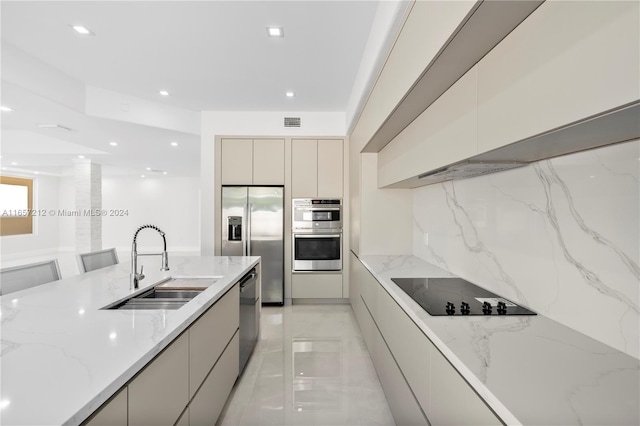 kitchen with cream cabinetry, stainless steel appliances, light stone counters, sink, and decorative backsplash