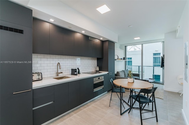 kitchen featuring sink, stainless steel oven, black electric cooktop, expansive windows, and backsplash