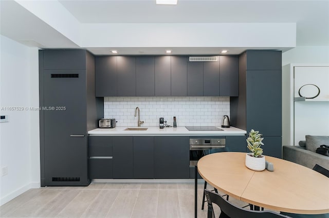 kitchen with stainless steel oven, gray cabinets, sink, and decorative backsplash