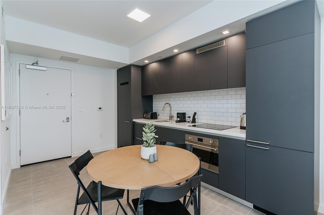 kitchen featuring sink, light tile patterned floors, backsplash, black electric stovetop, and oven