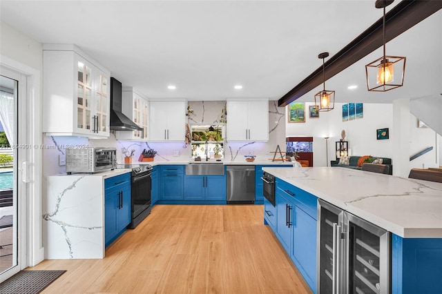 kitchen with white cabinets, blue cabinetry, decorative light fixtures, stainless steel appliances, and wall chimney range hood