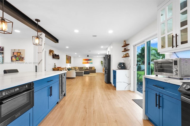 kitchen featuring light hardwood / wood-style flooring, decorative light fixtures, blue cabinetry, white cabinetry, and black fridge