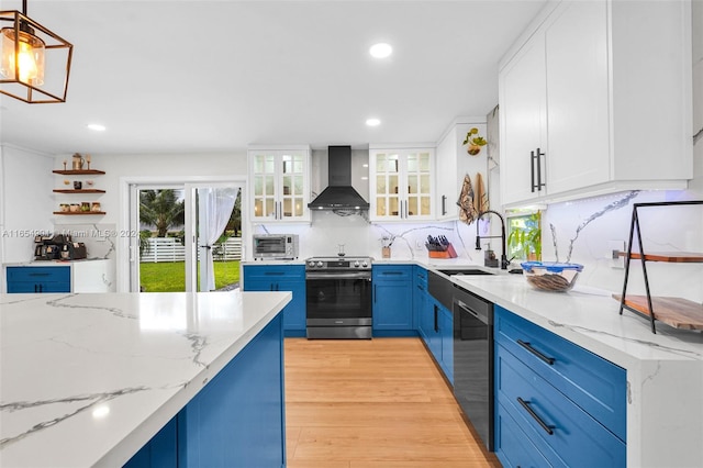 kitchen featuring wall chimney range hood, appliances with stainless steel finishes, decorative light fixtures, and white cabinetry