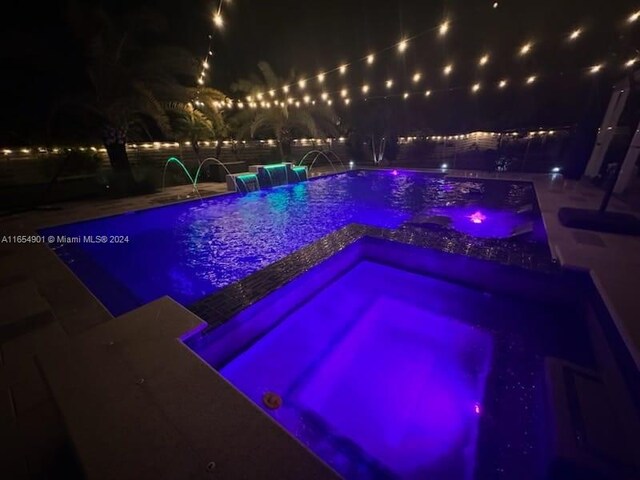 pool at night featuring pool water feature