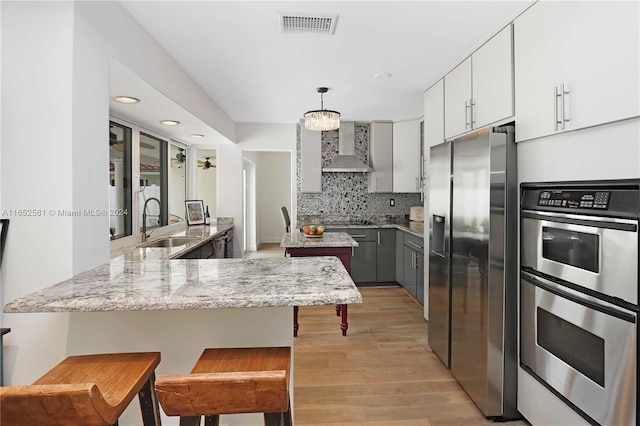 kitchen featuring wall chimney exhaust hood, a kitchen breakfast bar, kitchen peninsula, gray cabinets, and appliances with stainless steel finishes