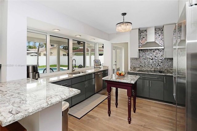 kitchen featuring wall chimney range hood, light hardwood / wood-style flooring, stainless steel appliances, sink, and decorative light fixtures