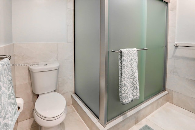 bathroom featuring a shower with door, toilet, tile walls, and tile patterned flooring