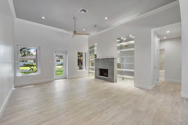 unfurnished living room with a tiled fireplace, ornamental molding, ceiling fan, a towering ceiling, and light hardwood / wood-style floors