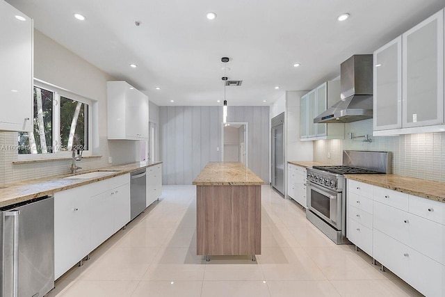 kitchen featuring white cabinets, hanging light fixtures, light stone countertops, wall chimney exhaust hood, and high quality appliances