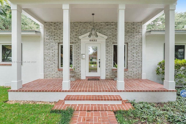 doorway to property featuring a porch and brick siding