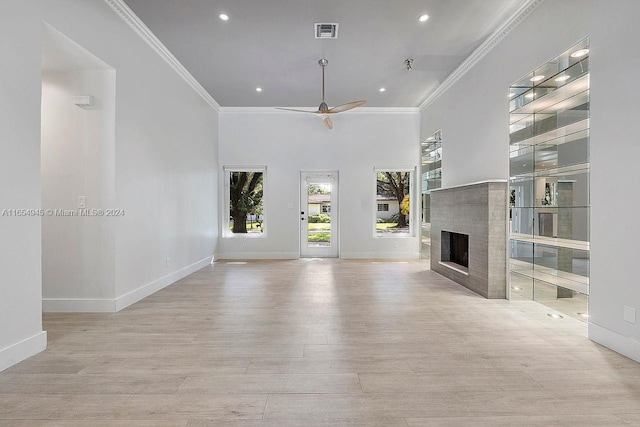 unfurnished living room featuring a tiled fireplace, light wood-type flooring, crown molding, and ceiling fan