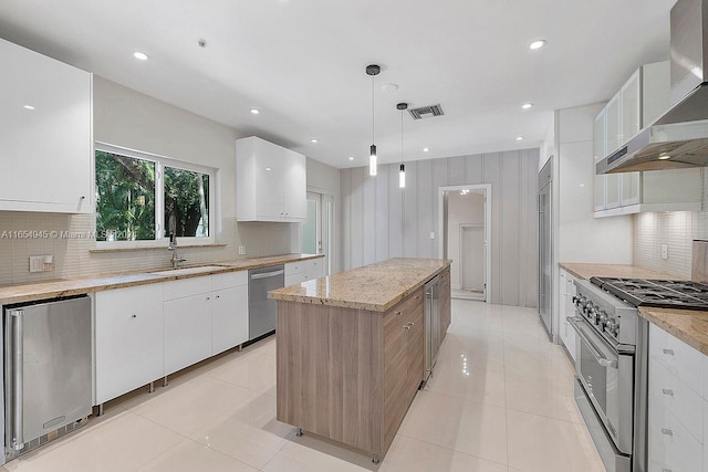 kitchen featuring light tile patterned floors, a kitchen island, a sink, appliances with stainless steel finishes, and wall chimney exhaust hood