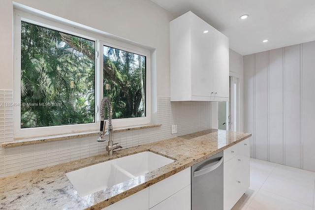 kitchen with light stone countertops, white cabinetry, a sink, decorative backsplash, and dishwasher