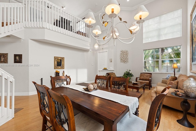 dining area with a towering ceiling, light wood-type flooring, crown molding, and a notable chandelier