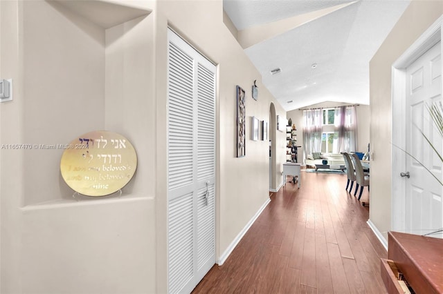 corridor with vaulted ceiling, a textured ceiling, and wood-type flooring