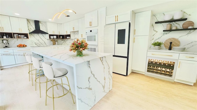 kitchen with white cabinetry, a center island, wall chimney exhaust hood, tasteful backsplash, and white appliances