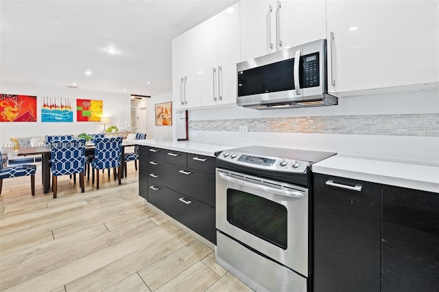 kitchen with decorative backsplash, white cabinets, light wood-style floors, appliances with stainless steel finishes, and dark cabinets