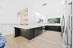 kitchen with visible vents, light wood finished floors, light countertops, stainless steel fridge, and dark cabinets