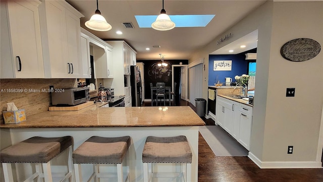 kitchen with a skylight, dark hardwood / wood-style flooring, kitchen peninsula, and white cabinets