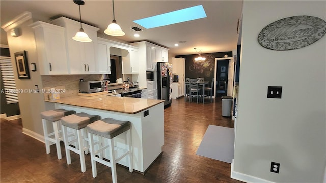 kitchen featuring a kitchen breakfast bar, pendant lighting, appliances with stainless steel finishes, kitchen peninsula, and white cabinets