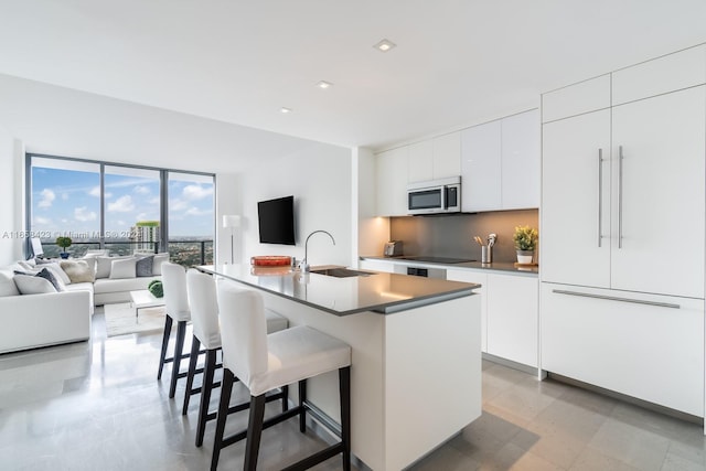 kitchen with white cabinets, sink, a kitchen island with sink, paneled fridge, and a breakfast bar