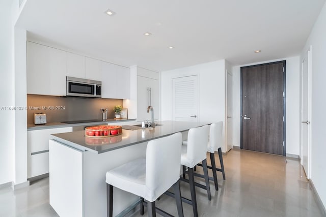 kitchen featuring an island with sink, black electric cooktop, sink, and white cabinets