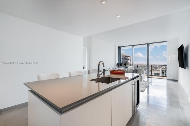 kitchen with white cabinets, a wall of windows, sink, beverage cooler, and a center island with sink