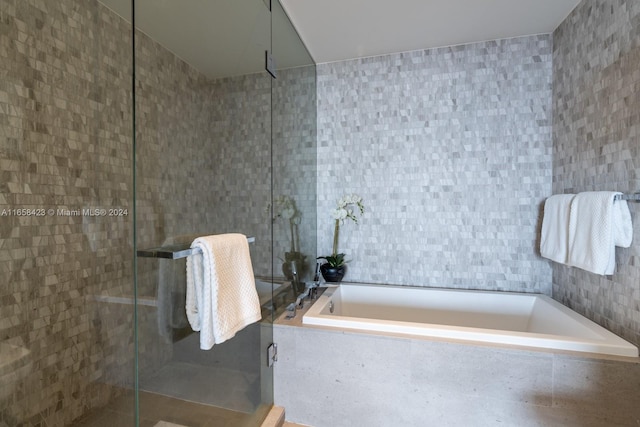 bathroom with shower with separate bathtub and tile walls