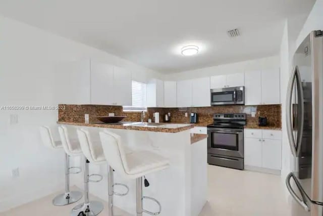 kitchen featuring a breakfast bar, backsplash, appliances with stainless steel finishes, and white cabinetry