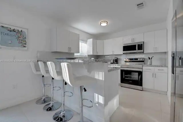 kitchen with white cabinetry, stainless steel appliances, a kitchen breakfast bar, light stone counters, and light tile patterned flooring