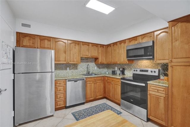 kitchen featuring light tile patterned floors, stainless steel appliances, sink, light stone countertops, and decorative backsplash