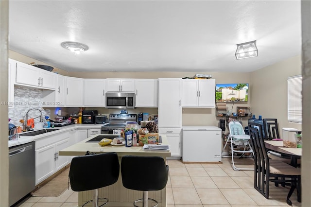 kitchen featuring light tile patterned floors, a center island, appliances with stainless steel finishes, white cabinetry, and sink