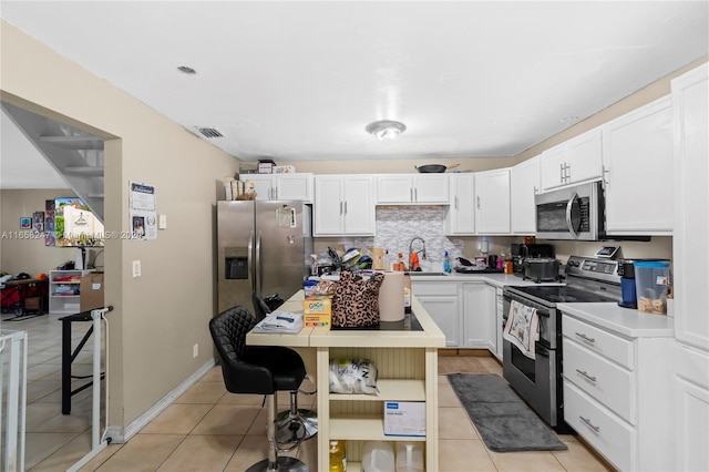 kitchen with light tile patterned floors, backsplash, appliances with stainless steel finishes, sink, and white cabinetry