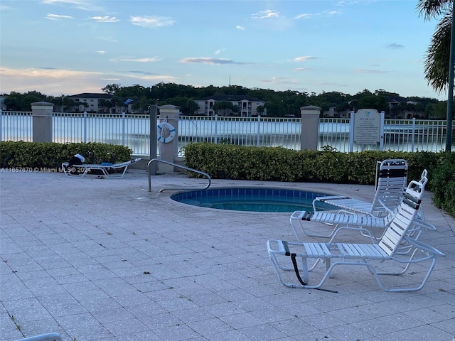 pool at dusk featuring a water view and a patio