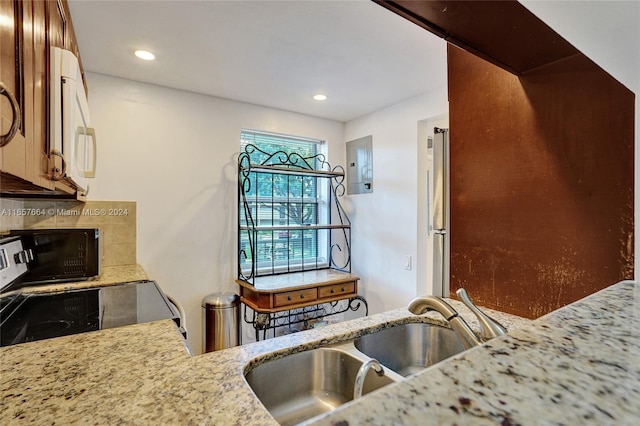 kitchen with light stone countertops, electric panel, backsplash, and sink