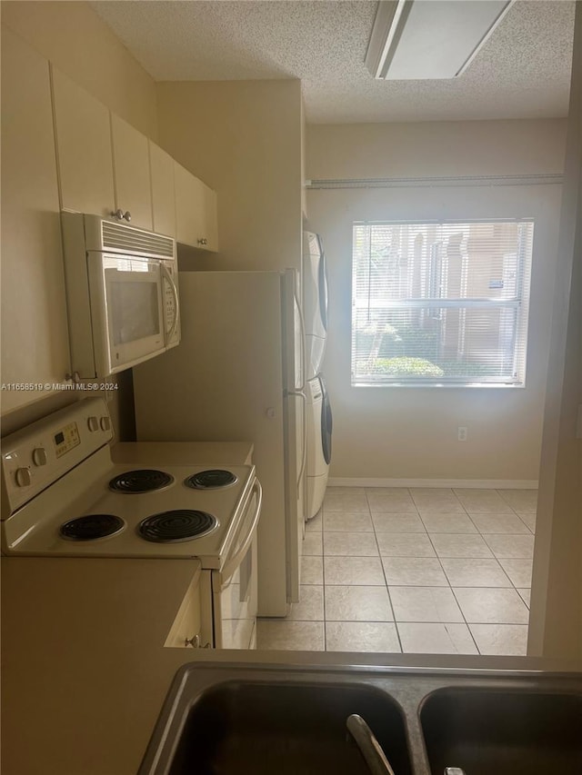 kitchen featuring a textured ceiling, white appliances, light tile patterned floors, stacked washer / dryer, and white cabinets