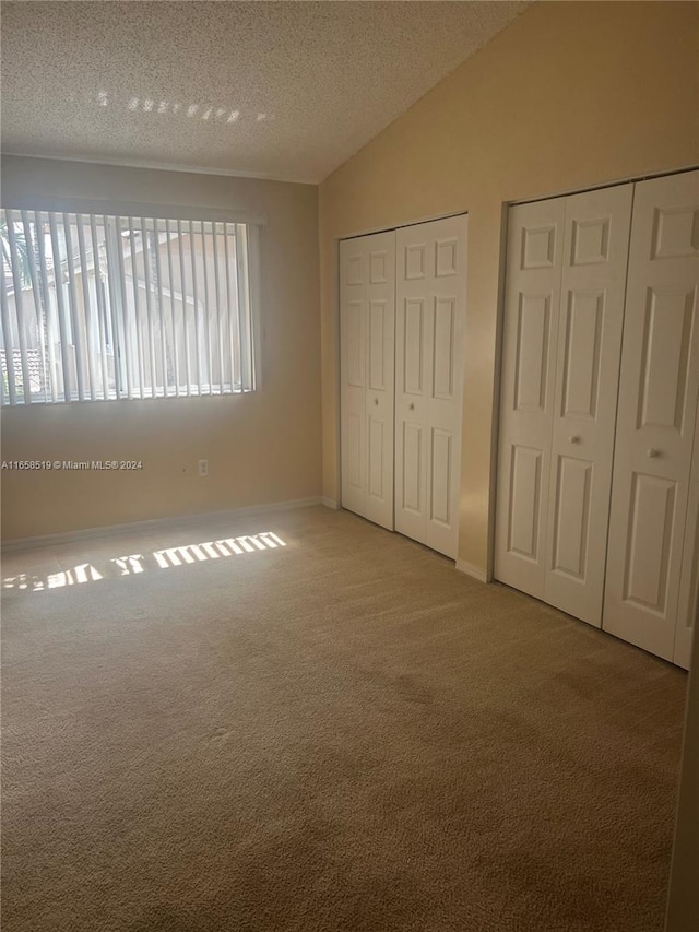 unfurnished bedroom featuring light carpet, vaulted ceiling, a textured ceiling, and two closets