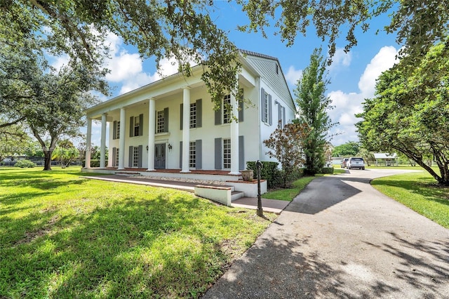 greek revival house with driveway, a front yard, covered porch, and stucco siding