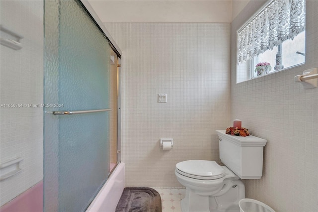 bathroom with tile patterned flooring, tile walls, toilet, and combined bath / shower with glass door