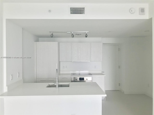 kitchen with cooktop, kitchen peninsula, sink, stainless steel oven, and white cabinetry