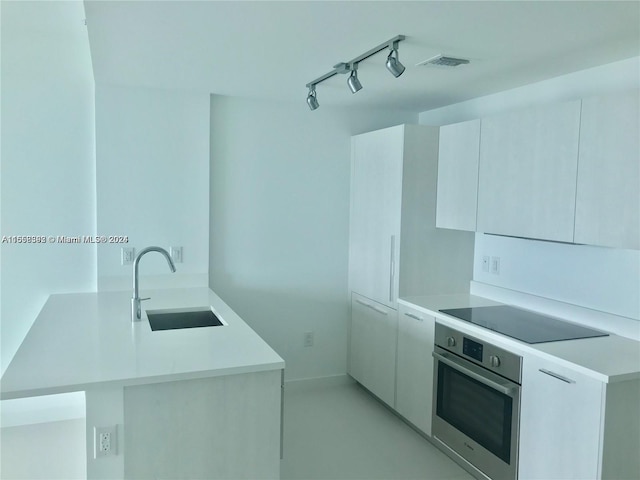 kitchen with kitchen peninsula, sink, stainless steel oven, white cabinetry, and black electric stovetop