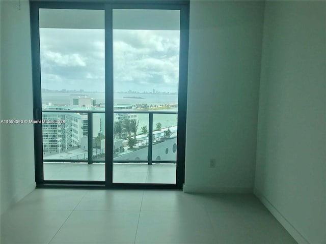 tiled empty room featuring a city view, a water view, and baseboards