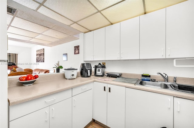 kitchen with a paneled ceiling, sink, and white cabinets