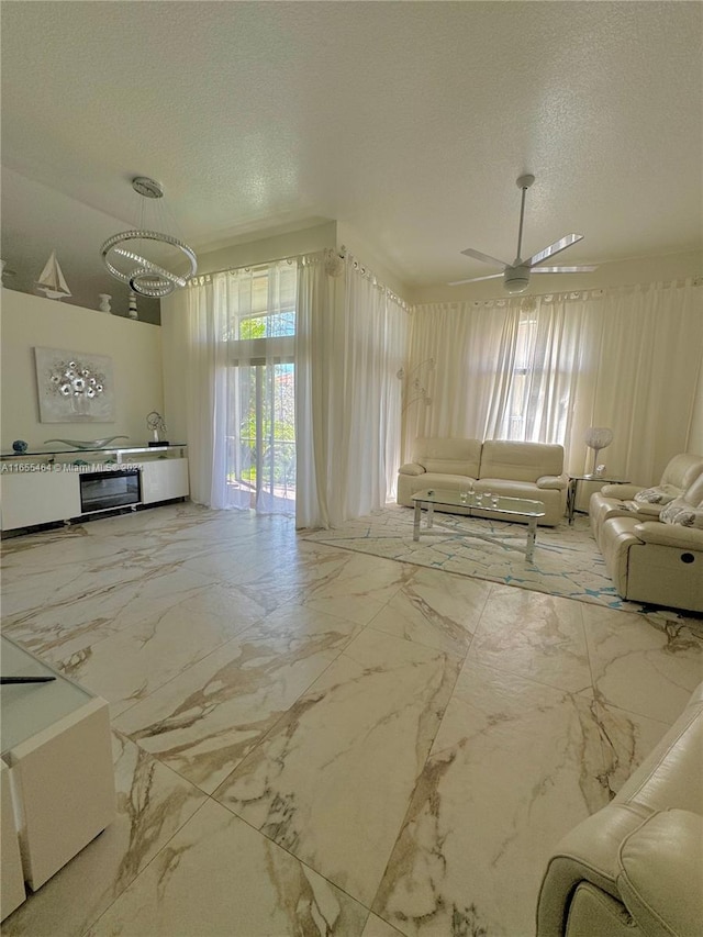 unfurnished living room featuring ceiling fan with notable chandelier and a textured ceiling