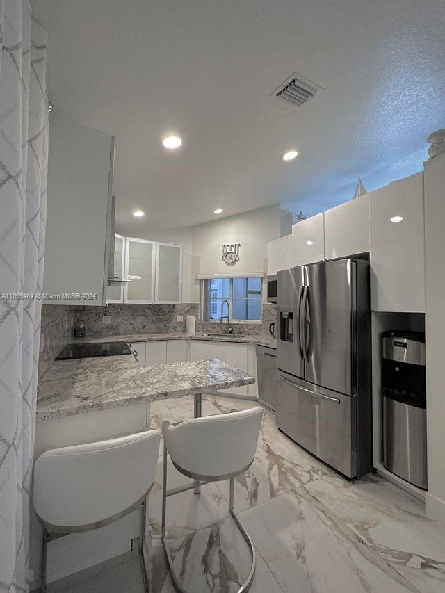 kitchen with appliances with stainless steel finishes, kitchen peninsula, backsplash, and white cabinets