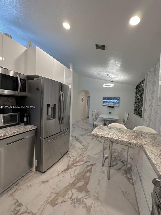 kitchen with a textured ceiling, stainless steel appliances, light stone countertops, and white cabinets