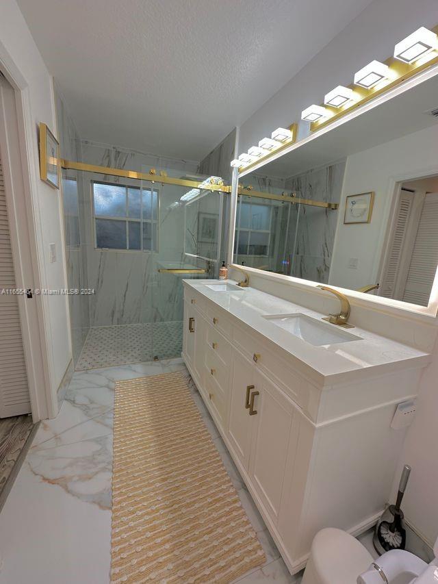 bathroom featuring vanity, toilet, a textured ceiling, and a shower with door