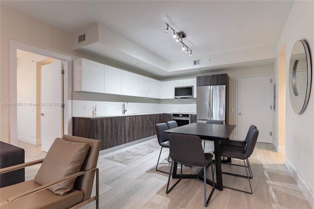 dining area featuring rail lighting, sink, and light hardwood / wood-style floors